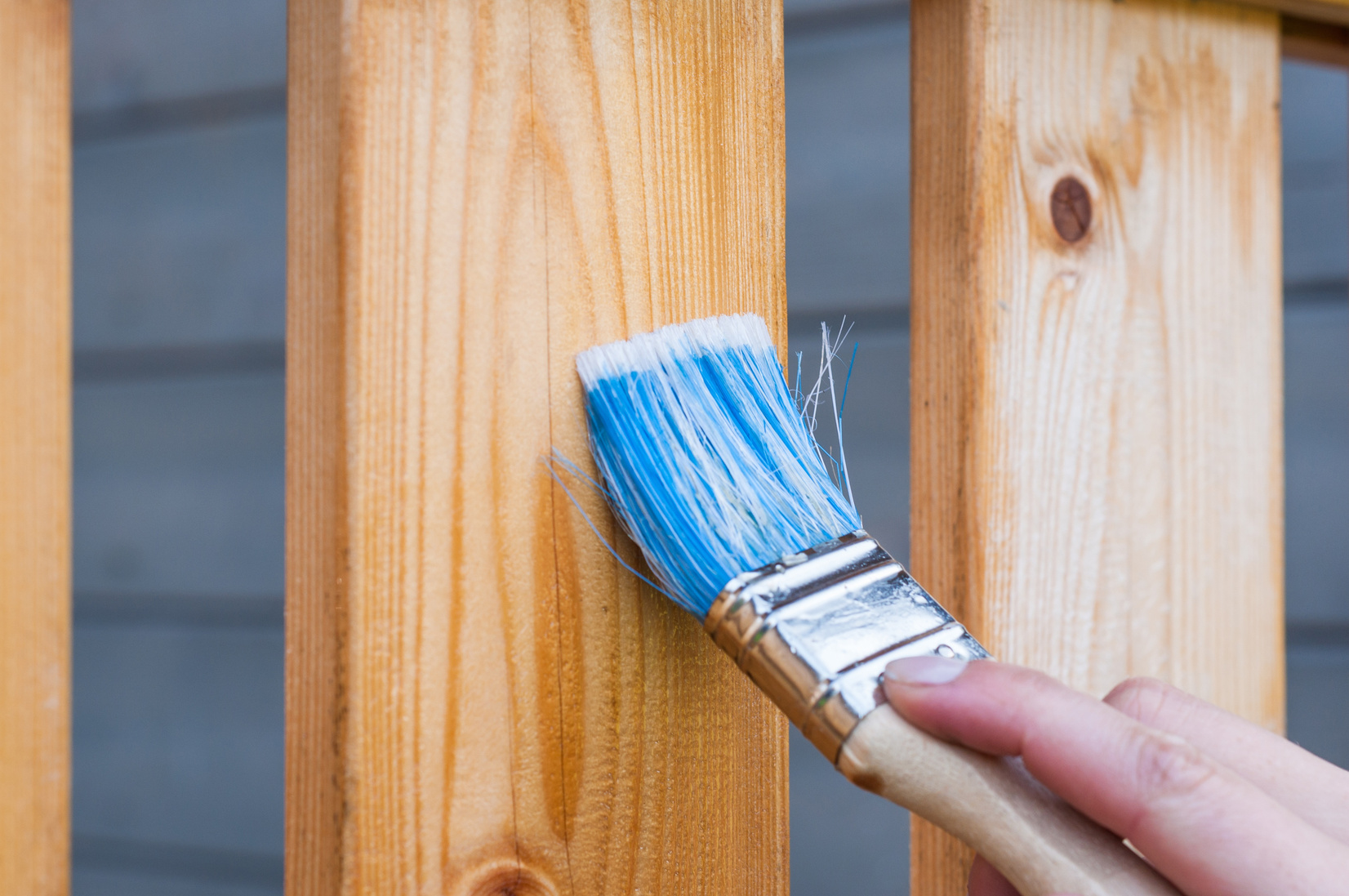 Paint brush applying blue paint to wood